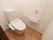 温水洗浄便座付きトイレで、便座横に操作ボタンがある。壁にL字型の手すりとナースコールが取り付けられている。