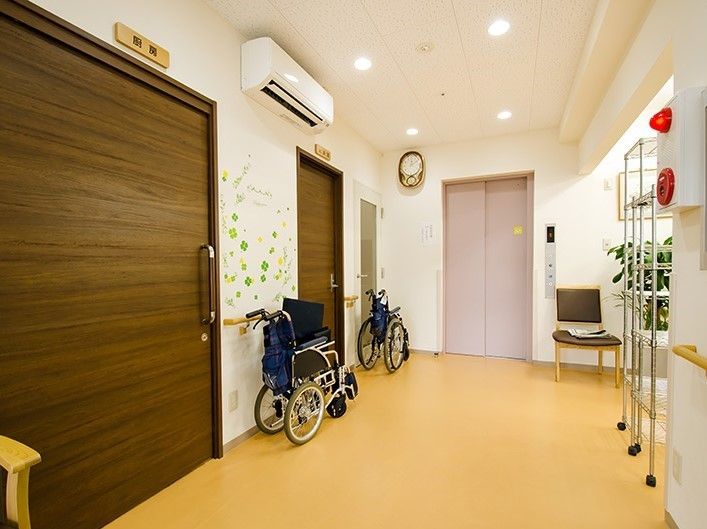 車椅子が置かれ、壁がクローバーで装飾された華やかな廊下。手すりが備え付けられており、扉は引き戸になっている。