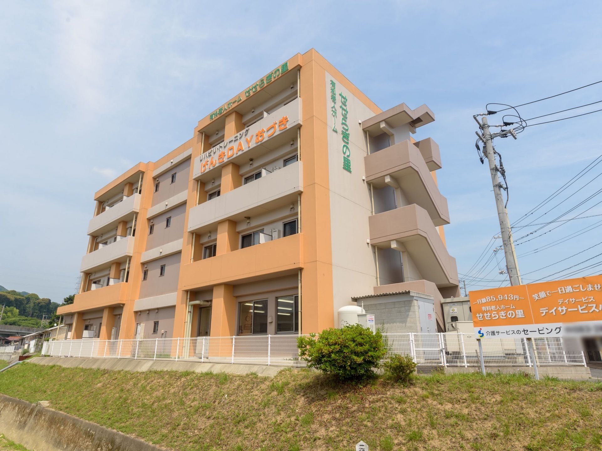 鉄筋コンクリート造りの４階建ての建物外観。外壁はオレンジ色とベージュ色をしている。外壁の上部には、施設名が大きく書かれている。