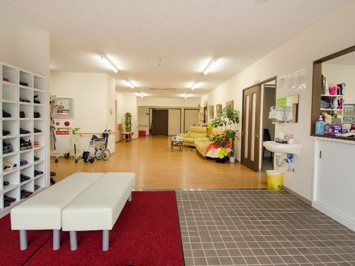 土間に敷かれた赤色の足ふきマットの上に２つのベンチがつなげて置かれている玄関内部