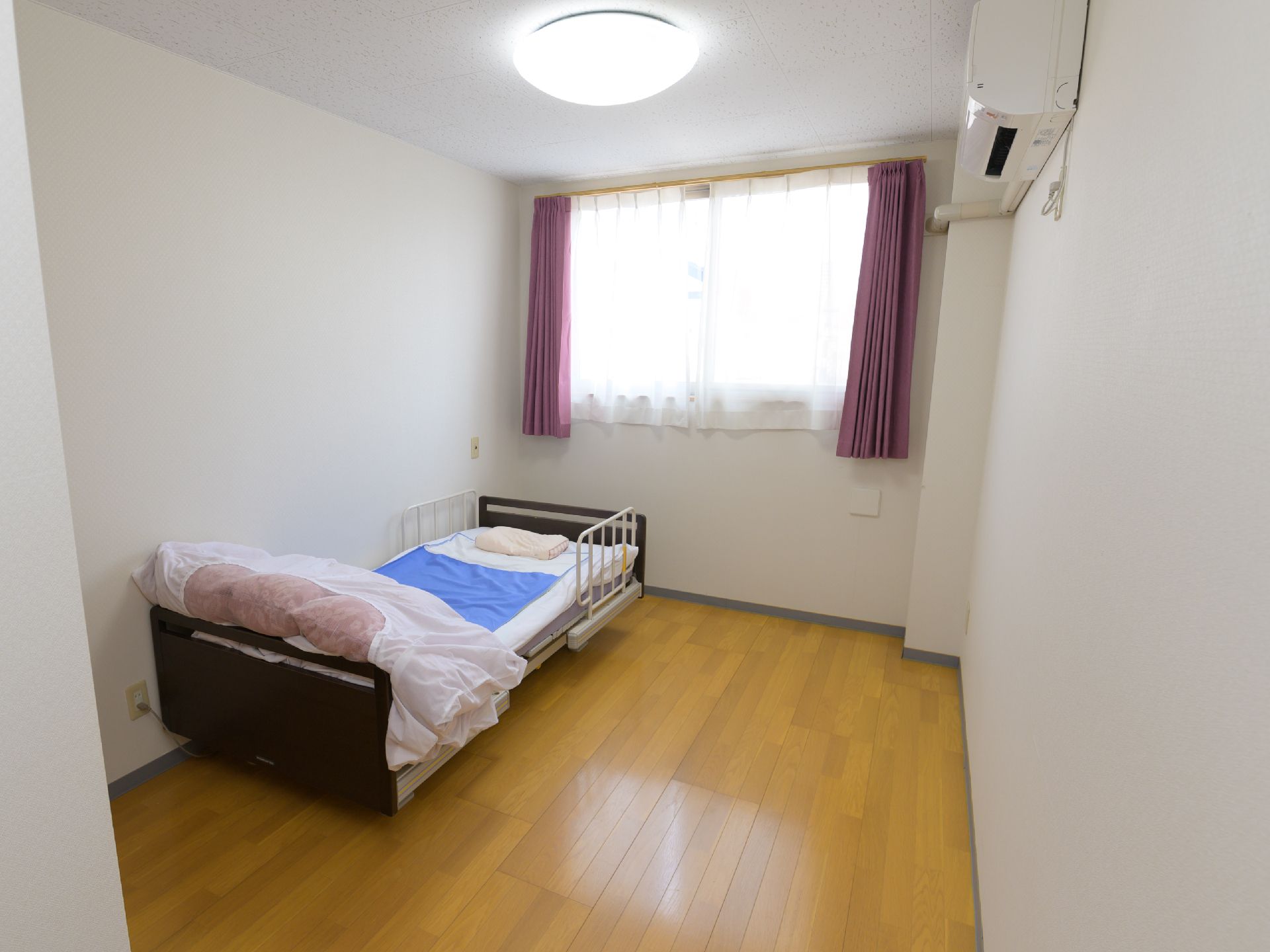 掛布団が折りたたまれて載っている、居室の壁際に置かれたベッド