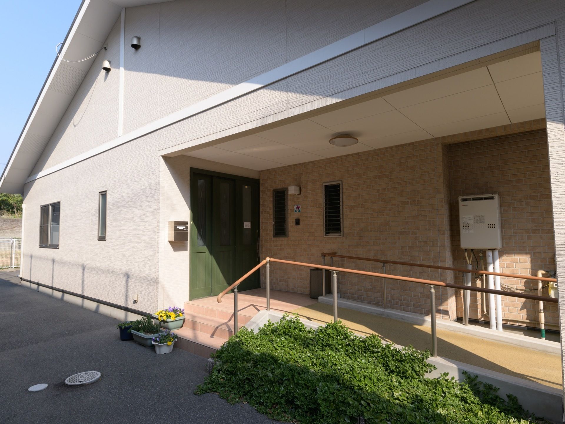 道路からゆるやかな勾配になっている入口である。屋根続きで手すり付きのスロープが完備されている。横には２、３段の階段がある。