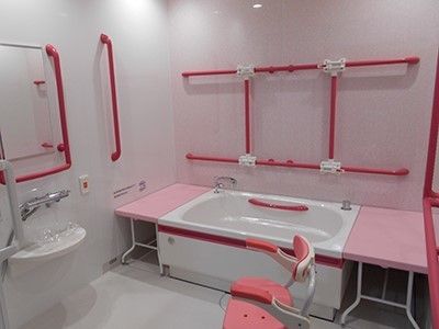 壁のいろいろな所に大きな赤色の手すりが設置されている浴室