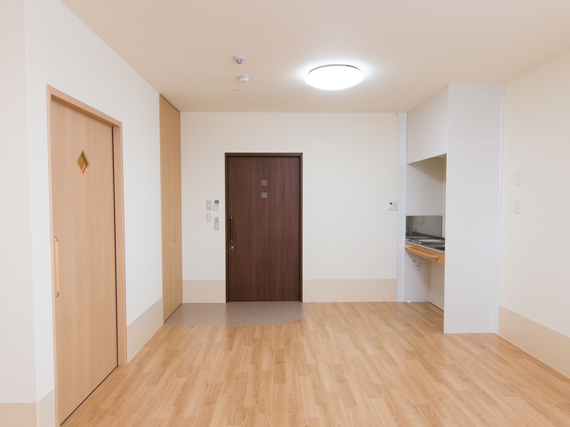 入口から段差なく入ることができるフローリングの居室がある。入口の横にはキッチンがあり、手すりが設置されている。