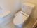 温水洗浄機能付きのトイレがある。入口は木製の引き戸になっていて、白い壁には手すりが備え付けられている。