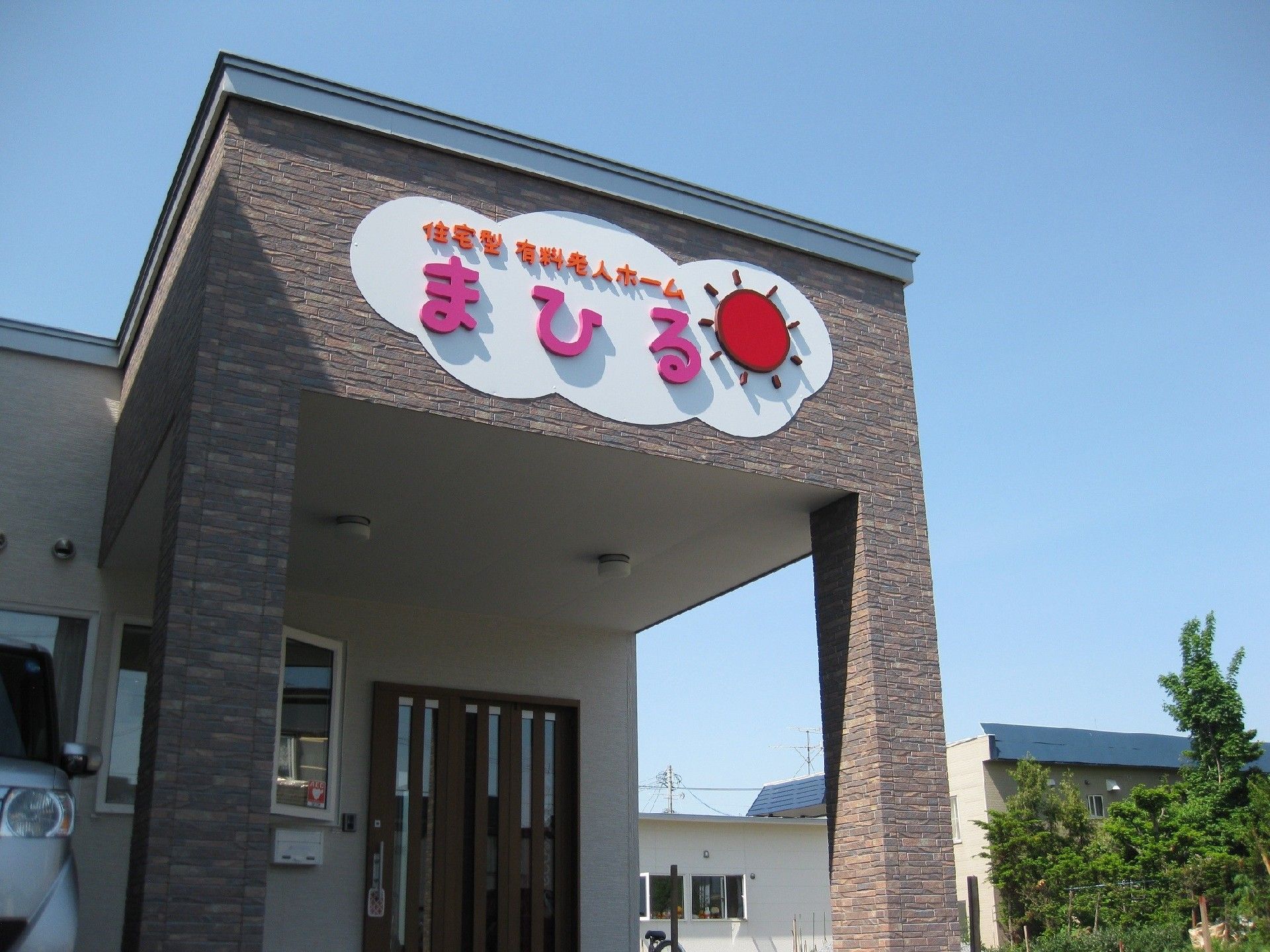 施設の入口の扉は幅が広く、上部は屋根に覆われている。屋根の前面には、施設の名称をかわいらしく表示した掲示が飾られている。