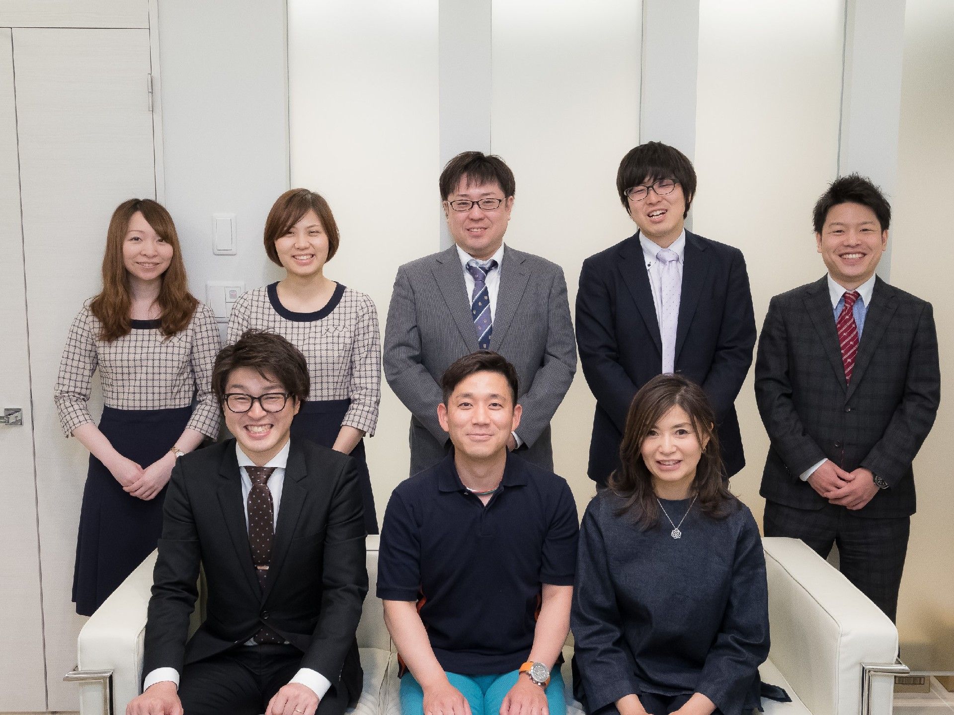 手前のソファに座っている３名、その後ろで立っている５名、合計８名のスタッフ