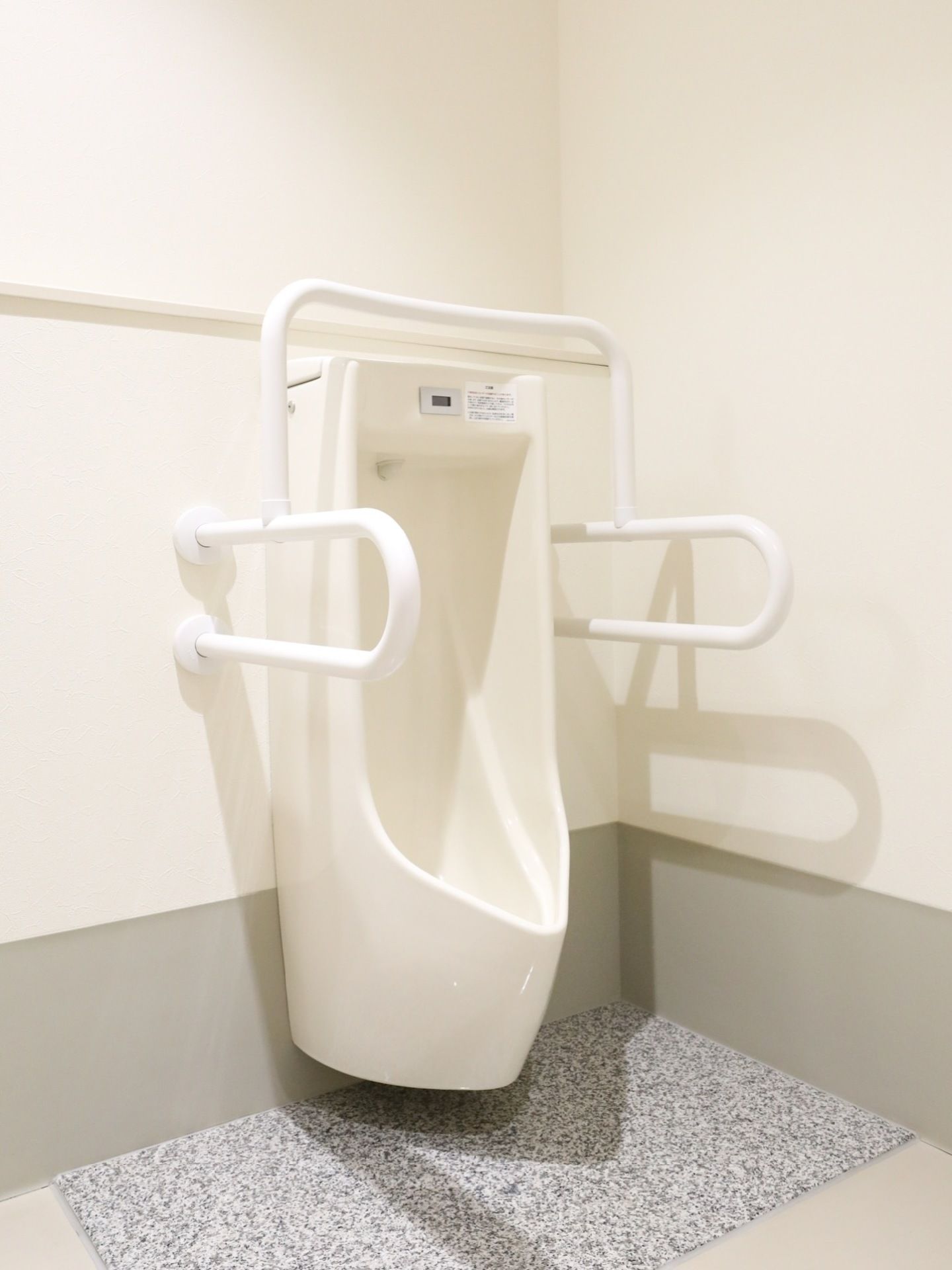 男性用のトイレは白を基調としたインテリアである。便器の両脇と上部には移動などをサポートする手すりを設置している。