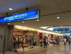 駅地下街の様子。洋服屋などの店舗が立ち並び、天井にはポスターや電車乗り場の青い看板が設置されている。