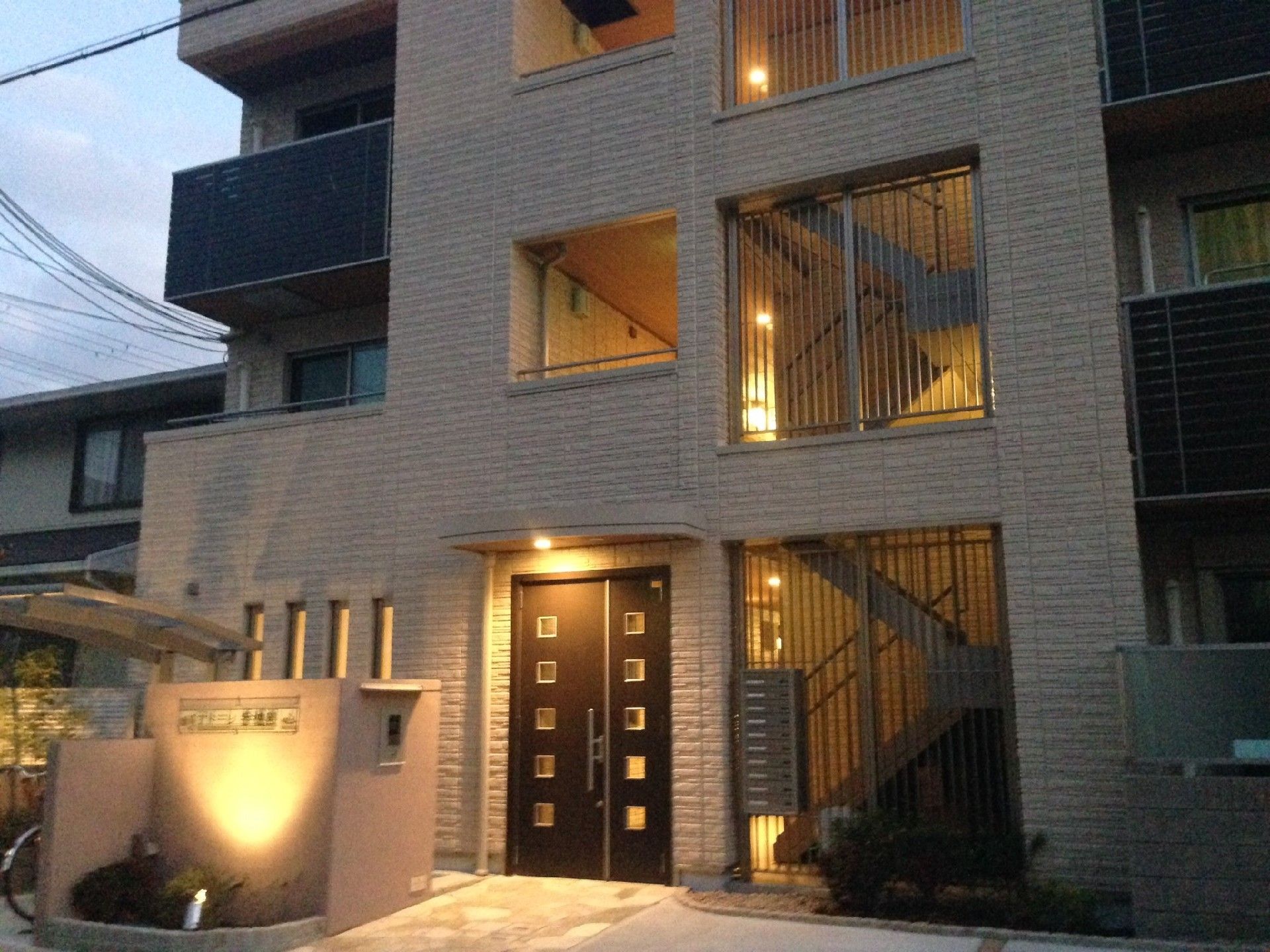 門柱の正面は、下からスポットライトが当たるようになっている。3 階建ての建物は、玄関ひさしや廊下の各所に、照明が付けられている。