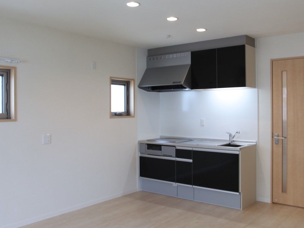 壁や天井が白で統一された室内には、IHコンロのシステムキッチンが設置されている。キッチン上部には棚と換気扇があり、壁には小窓が２つある。