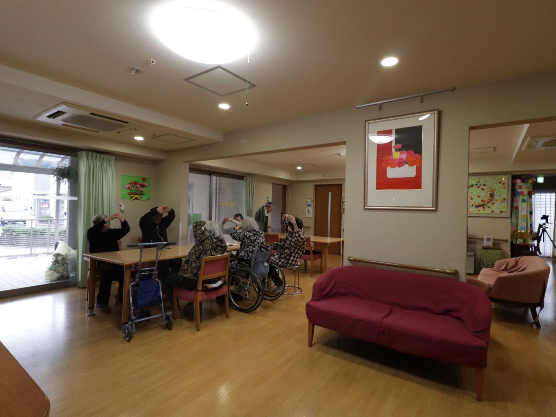 入居者様がお食事を取る長テーブルがある。健康を心がけて、座ったまま無理のない範囲でストレッチをしている。