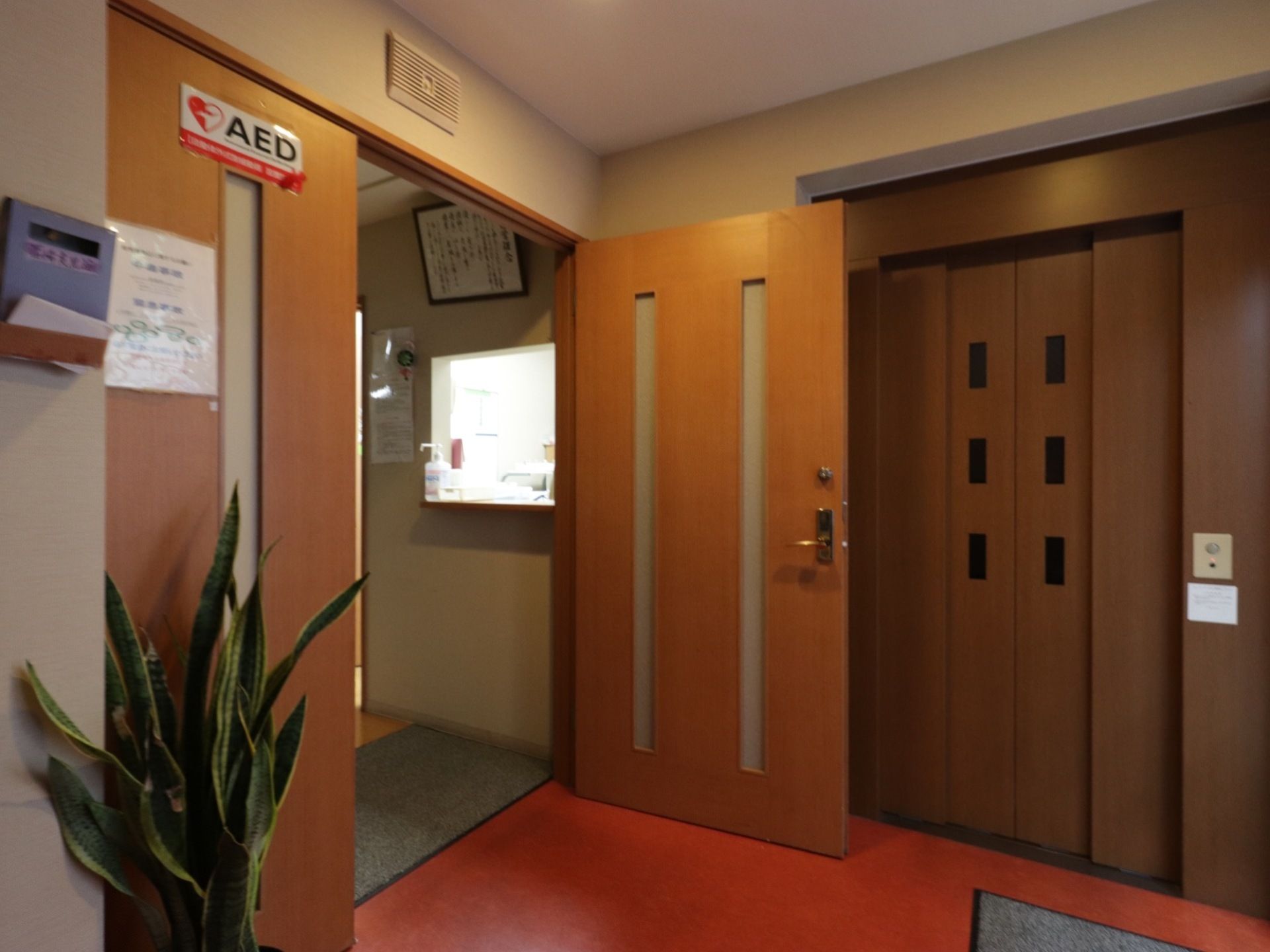受付は、エレベーターの隣にあるドアを越えた場所にある。受付には木製のカウンターがあり、手指消毒用の消毒液を用意している。