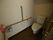 洋式便器が備わった個室トイレである。壁には縦型の手すりと横型の手すり、さらに呼び出しブザーが備わっている。