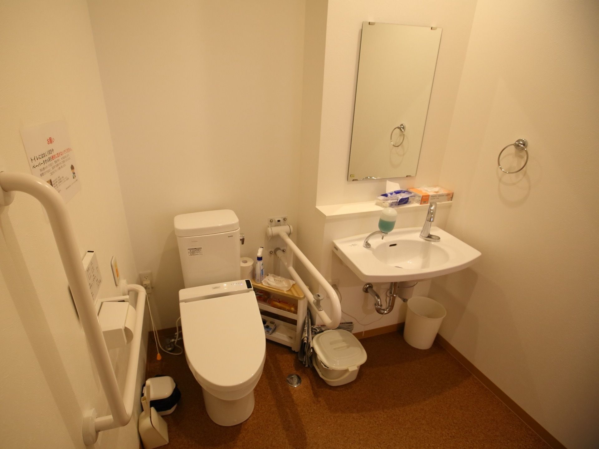 共用トイレにふたつきの便座がある。その隣には、自動水栓の洗面台があり、壁にはタオルホルダーがかかっている。