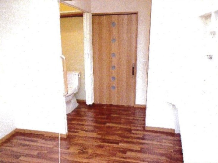 真っ白な壁とブラウン系のフローリングがオシャレな居室。扉は引き戸になっている。トイレも設置されていて、カーテンで区切られている。