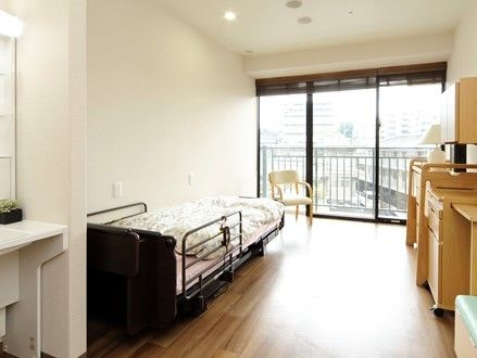 横一面がガラス張りで、明るい空間を確保した居室である。壁際に介護用ベッドやインテリア家具などを配置している。