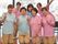 施設の大きなガラス窓の前にて、様々な年齢層のスタッフがピンクとブルーのお揃いの制服で2列に並んでいる。笑顔で手をVの字にしている。