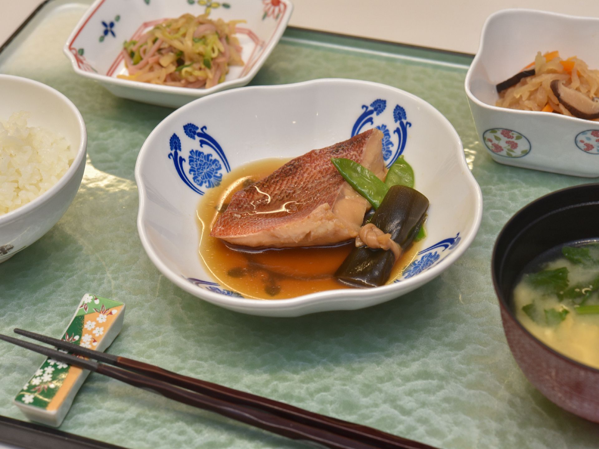 ある日の献立は、米飯、味噌汁、主菜は煮魚、副菜に切り干し大根の煮物と酢の物であった。煮魚の付け合わせは昆布巻きとさやいんげんである。