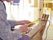フローリングの部屋に複数の椅子がある。入居者様が道具の前に座り、糸を組んでデザインを作る作業をしている。