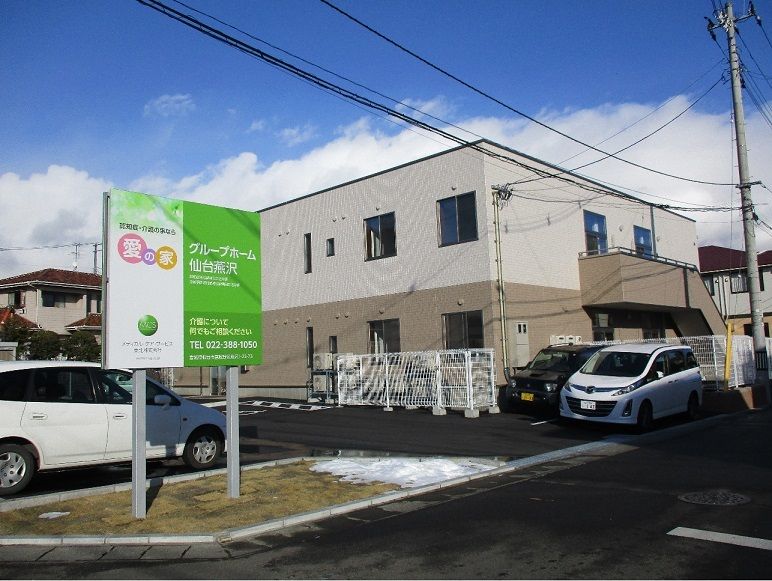ブラウンとベージュ色の落ち着いた色合いのグループホームである。建物の２階部分から階段が設置されている。