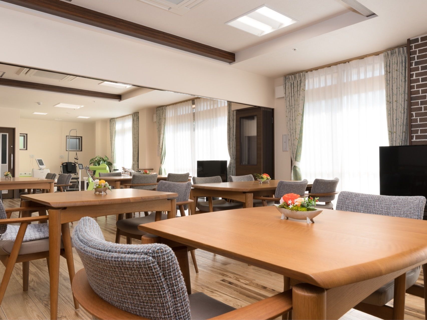 窓のある広い部屋にはテーブルと肘掛けつきの椅子、テレビが置いてある。奥には、機能訓練に使用する機械も設置されている。