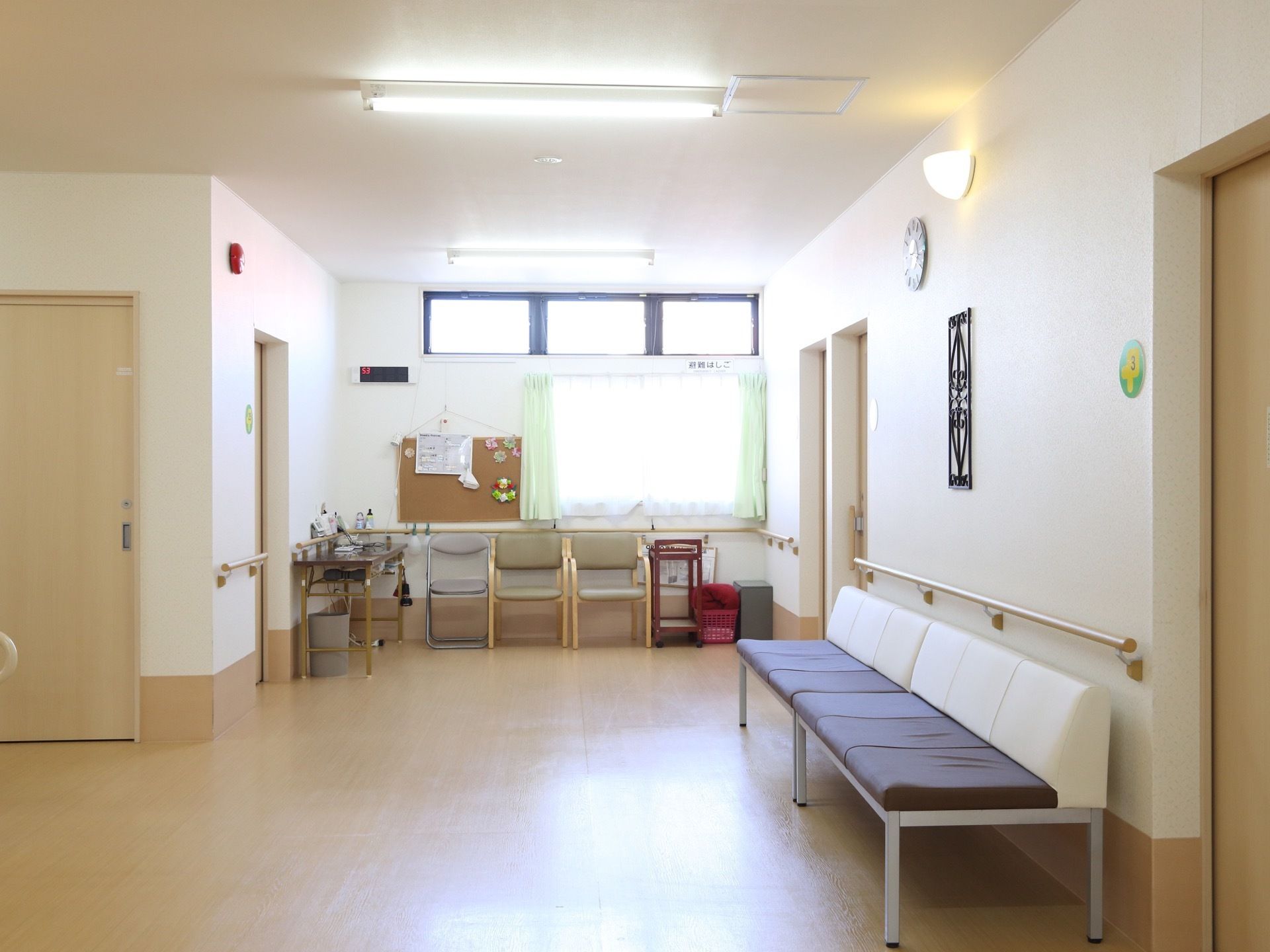 通路に置かれたベンチや椅子。高い位置に明り取りの窓、その下に普通の窓がありとても明るい。壁面には手すりを設置。