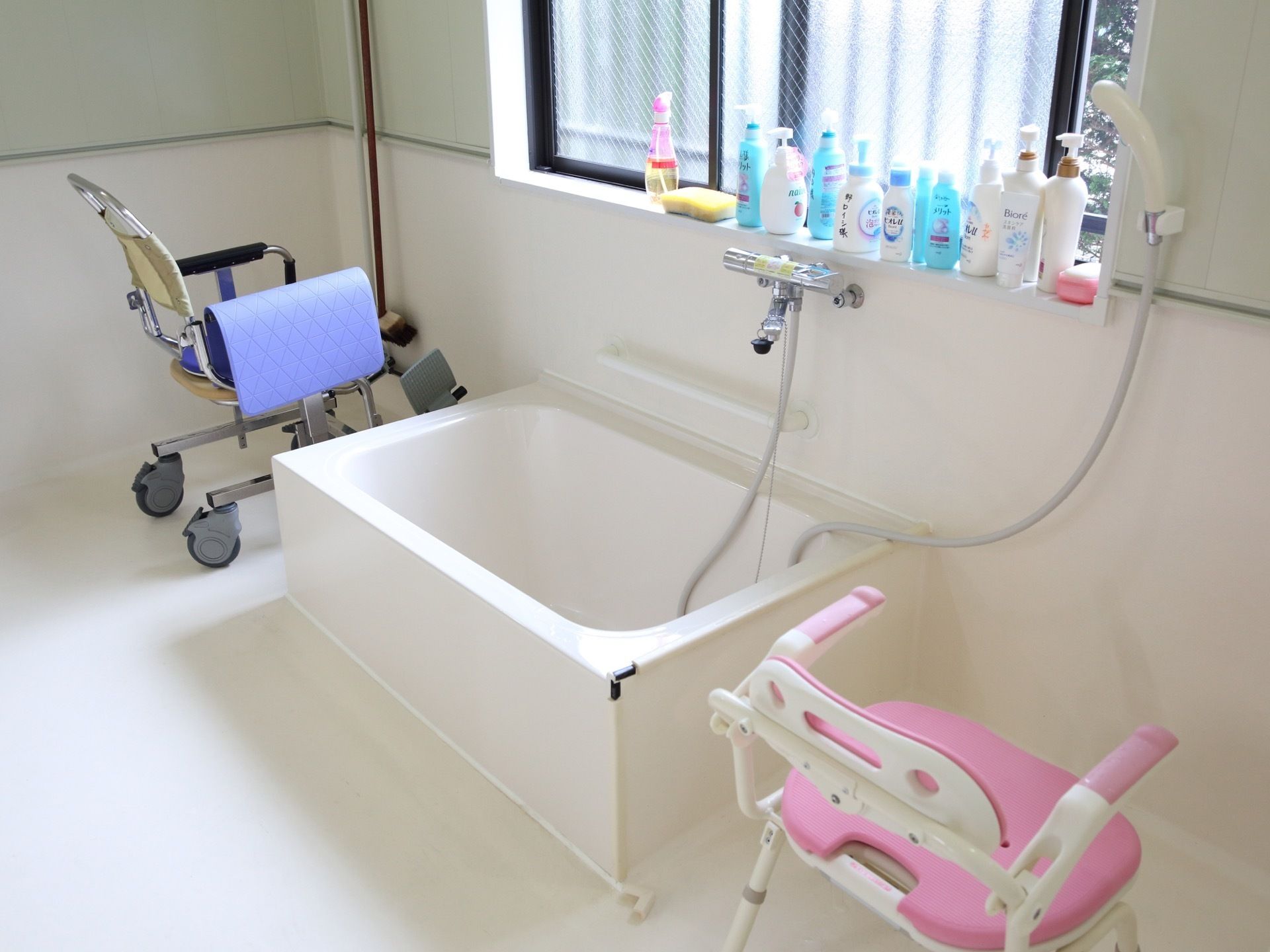 浴室の浴槽の両側にはお風呂用の椅子が置かれている。窓際には入居者様用のシャンプーなどが並べられている。