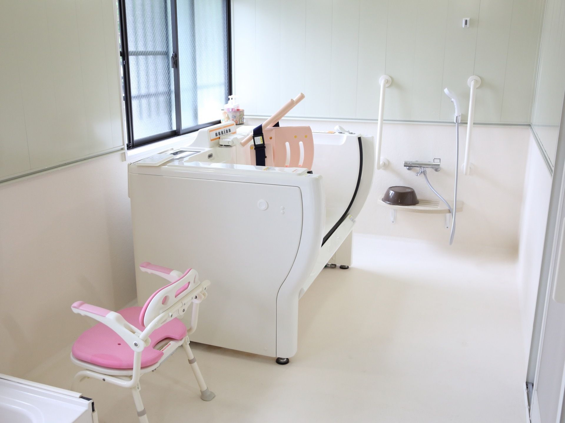 浴室には介護用入浴機器を設置している。また、洗い場にはピンク色のお風呂用シャワーチェアーや洗面器もある。