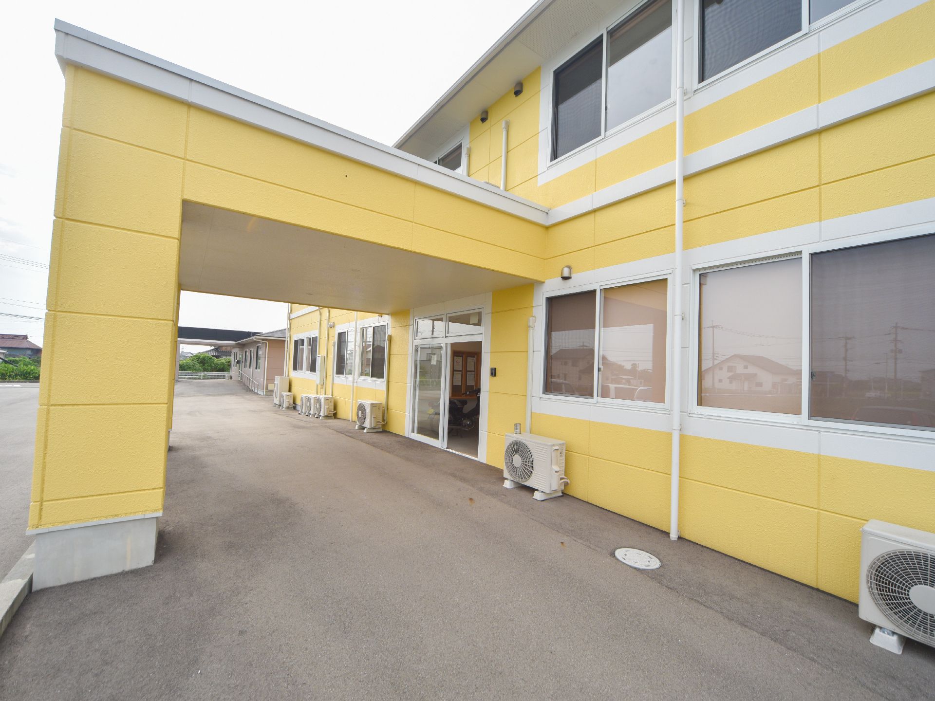 2階建てになっていて、外壁は黄色と白である。玄関前はとても広く、段差もないので、車いすの方の移動も安全にできる。