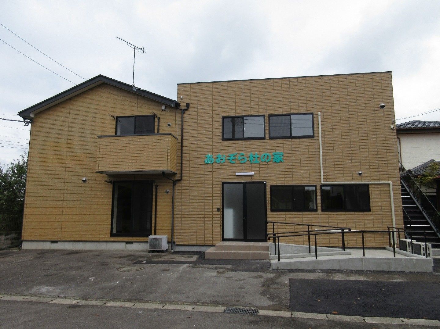 木造２階建て。玄関アプローチにはスロープと手すりを設置し、車椅子をご利用の方が安全に移動できるよう配慮している。