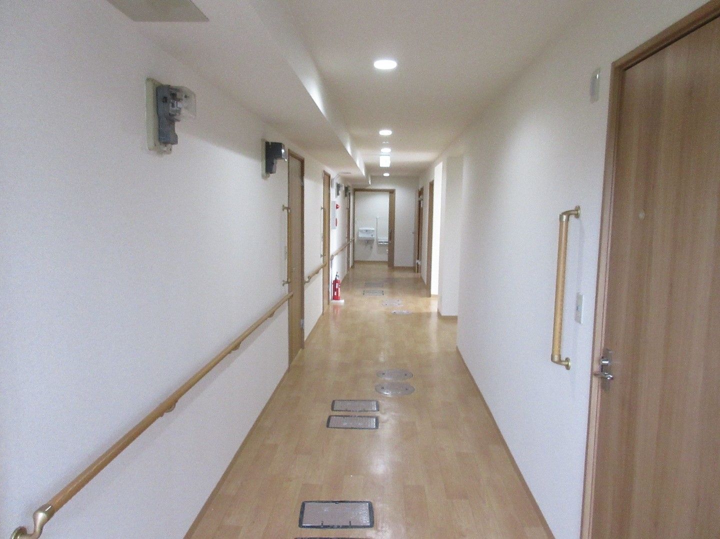 木製のドアが立ち並ぶ廊下で、左側にのみ手すりが設置されている。床は板張りだが、随所に石のタイルがはめ込まれている。