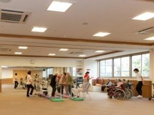 一面の腰高窓の下に、車椅子に座った入居者様が複数おられる。前後にスタッフが立ち、声をかけて手拍子を打っている。