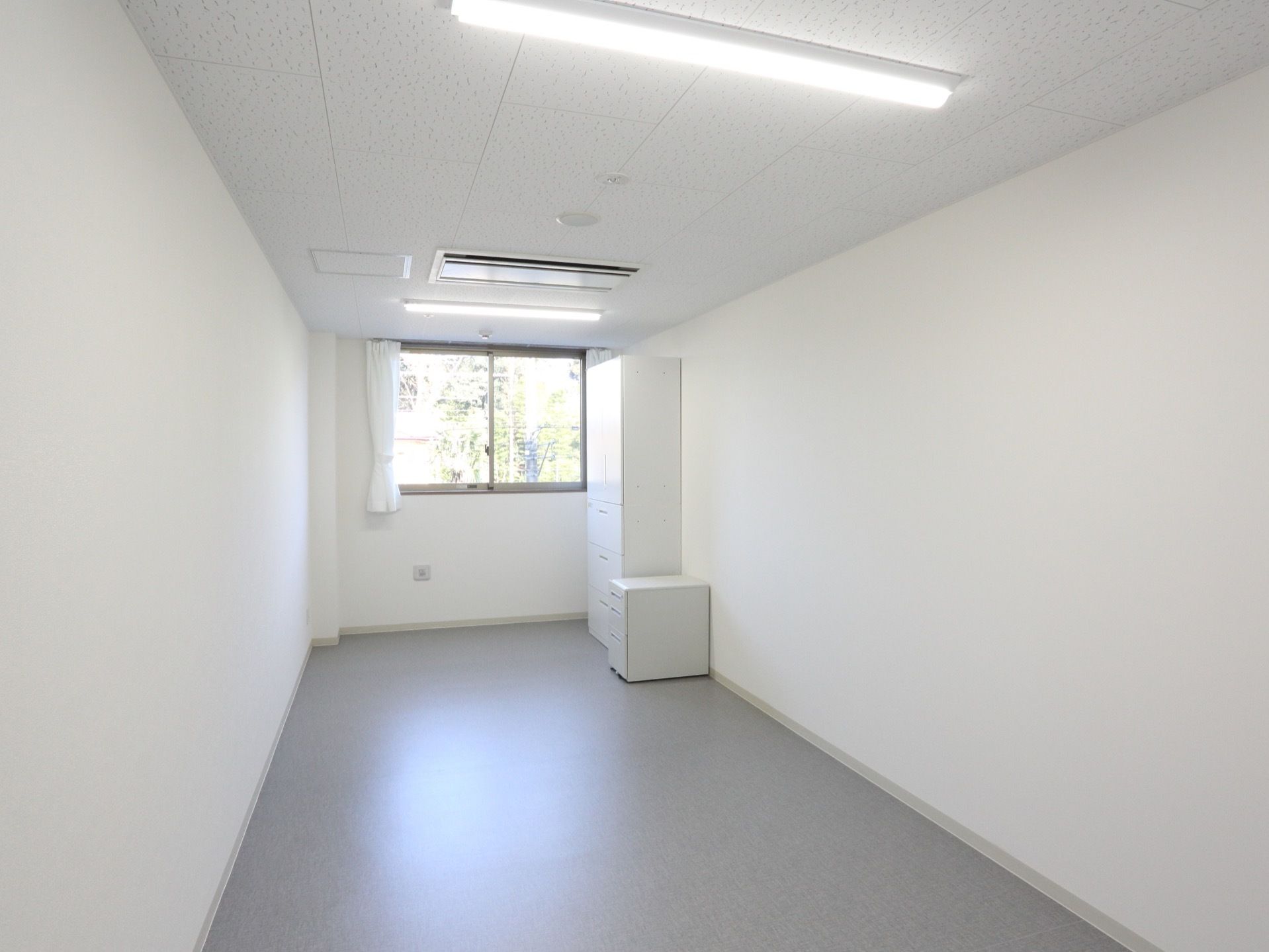 居室は白を基調としたシンプルなインテリアである。床は全面フラットで、壁にはカーテンを掛けた腰高窓を一つ設けている。