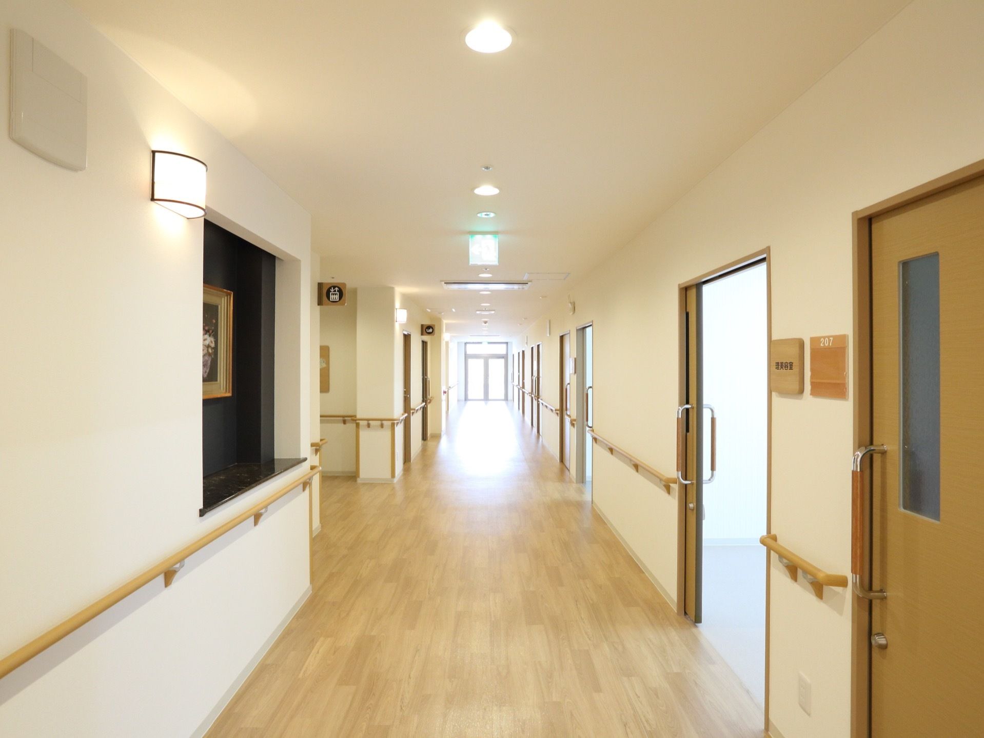 通路の両側には居室のドアが並び、壁には名前用のプレートを取り付けている。天井には複数の照明を設置している。