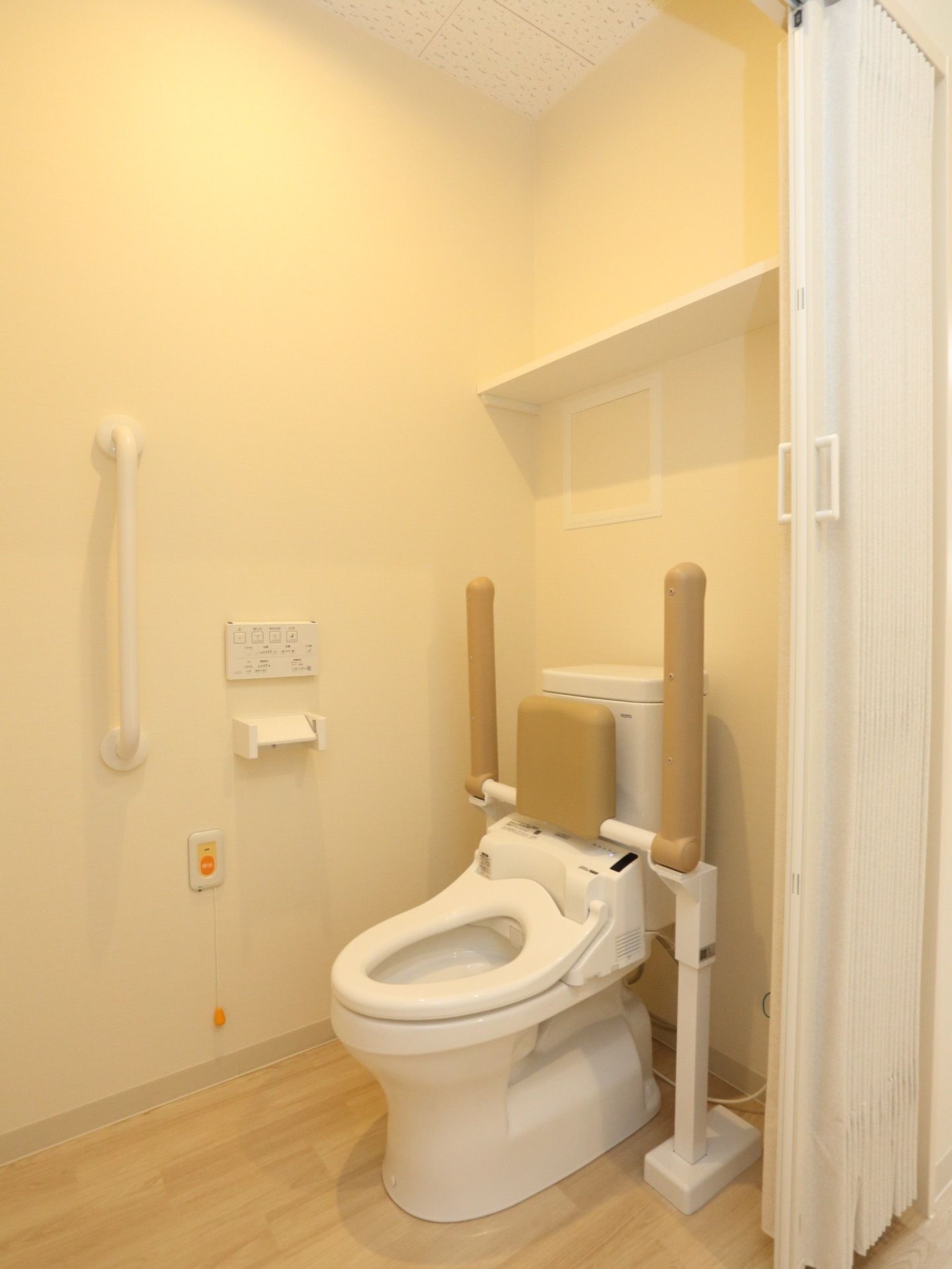 トイレの出入り口はアコーディオンドアである。内部の壁には手すりとナースコールを設置し、上部には棚を取り付けている。