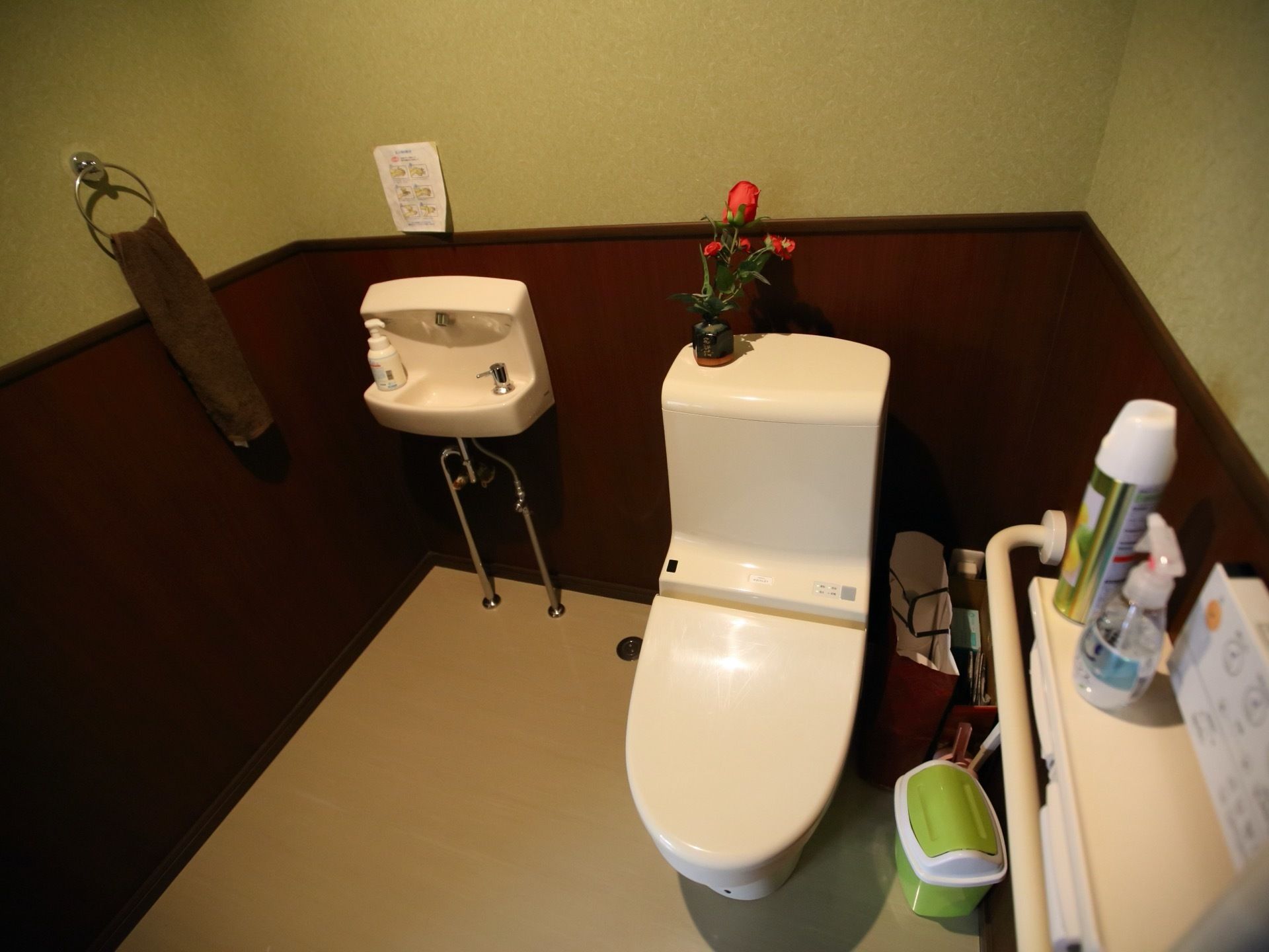 トイレと洗面台が同一空間に設置されている。ペーパーホルダーの上には消毒液や消臭剤などが置かれている。床の上にはごみ箱がある。