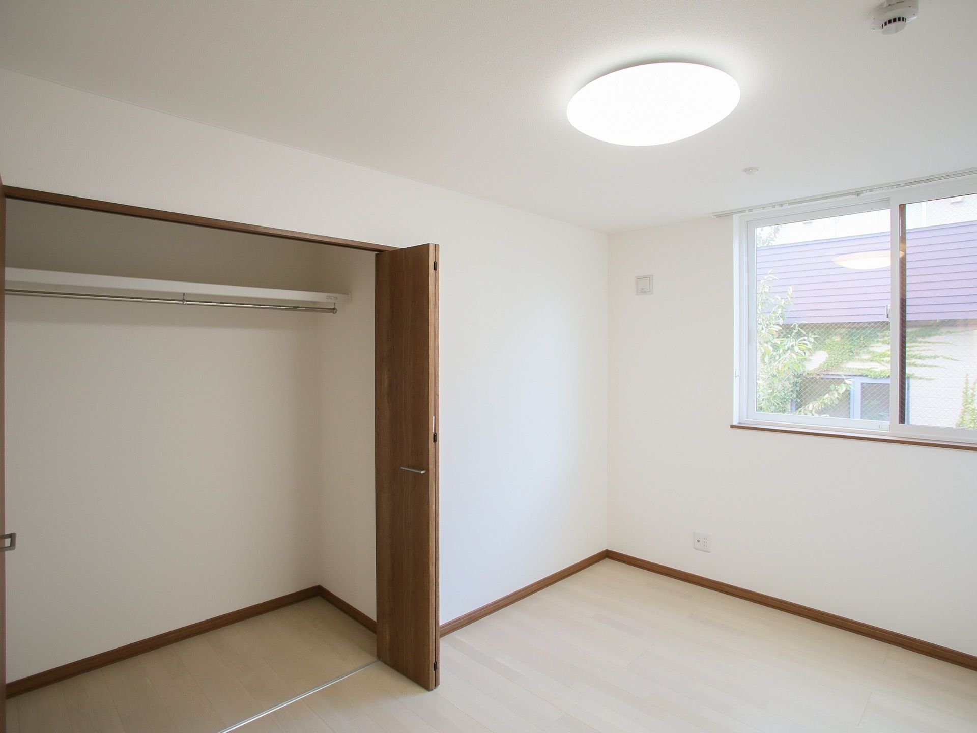 白を基調とした広くて明るい空間になっている。木目調のクローゼットの扉が開いており、中には洋服が下げられるポールがついている。