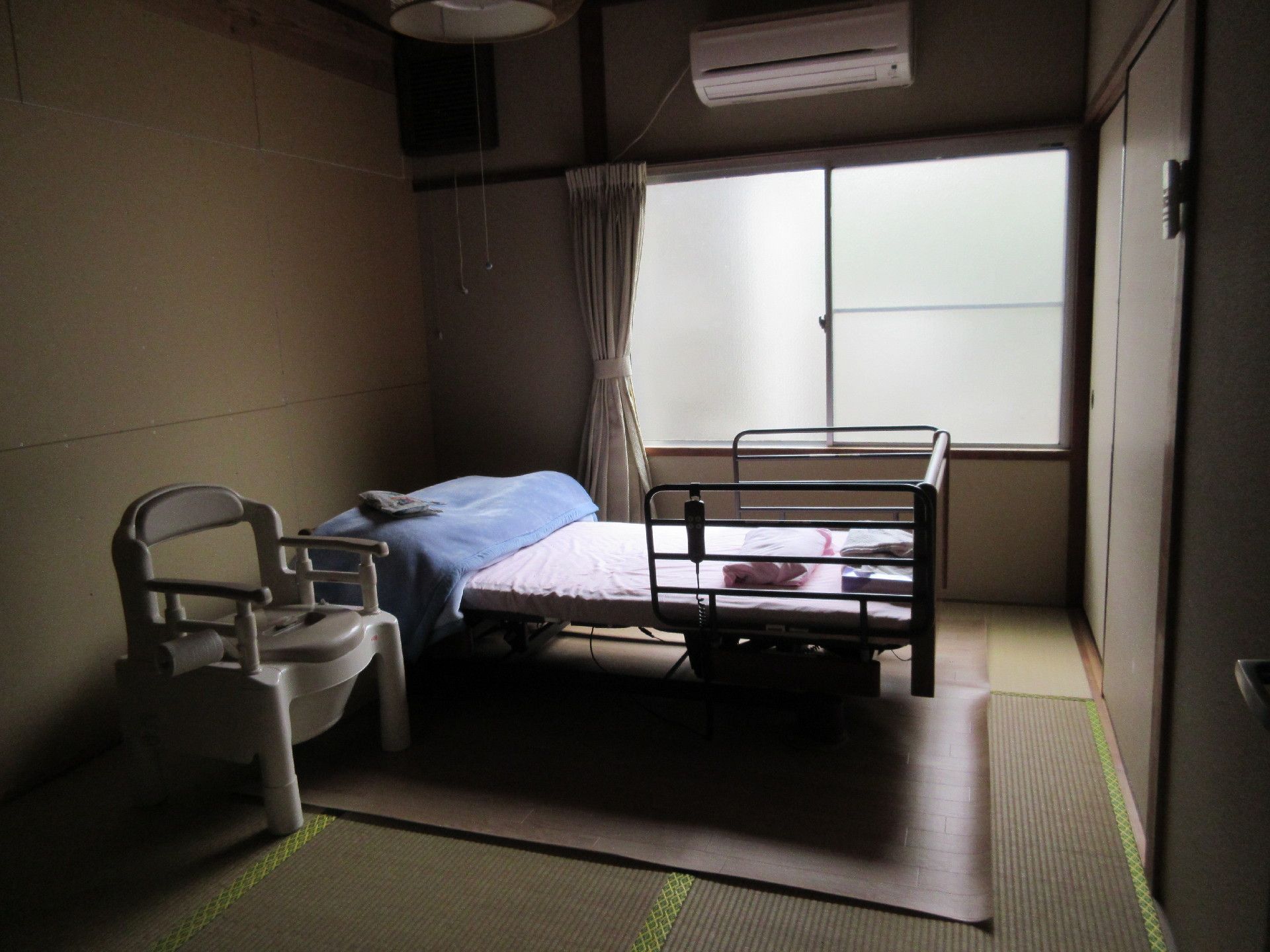 畳敷きの和室で、腰高窓がある。介護ベッド、椅子、エアコンが完備されている。ふすまの収納が付いている。