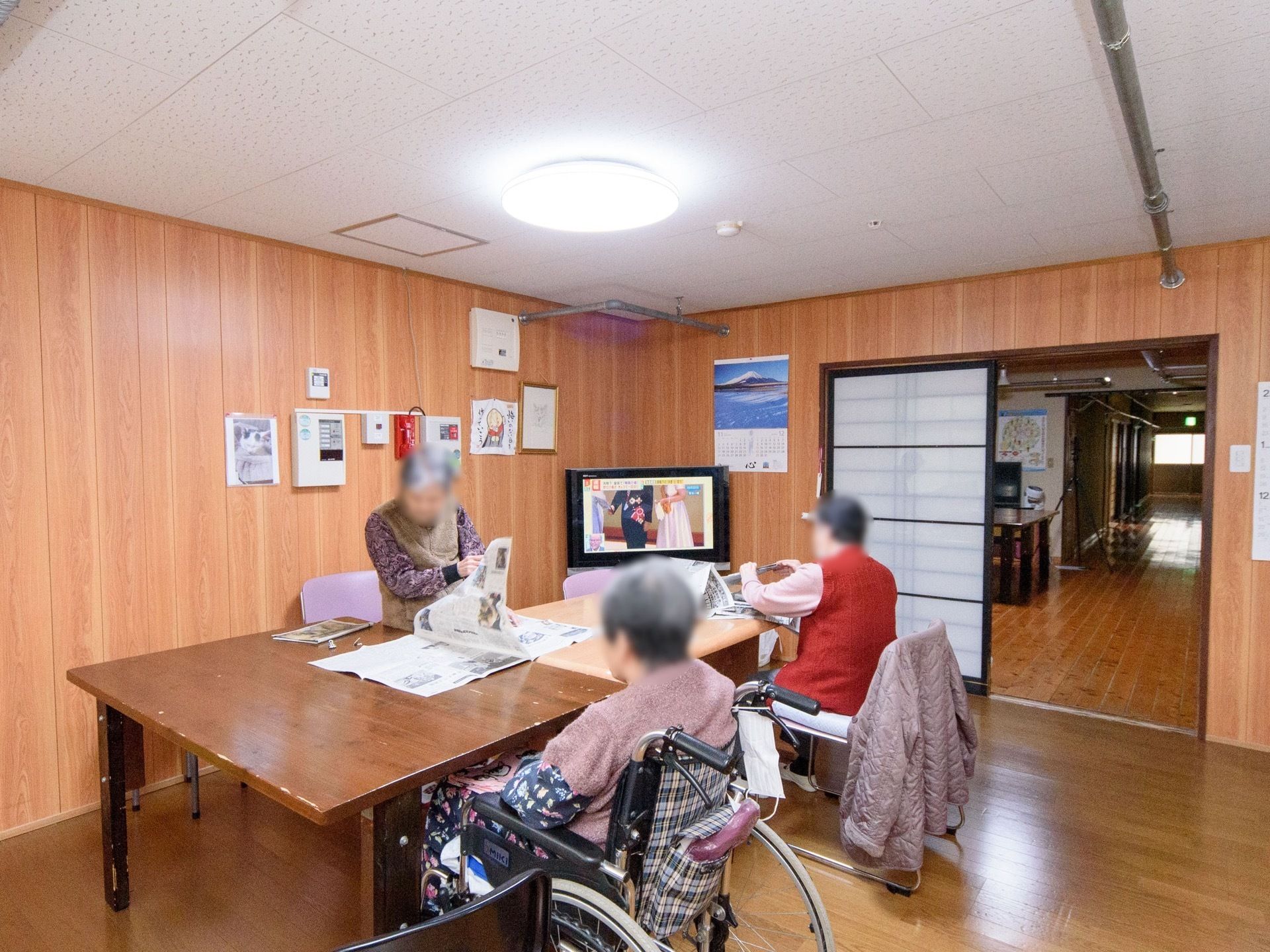 大きなテーブルが置かれ、その周囲に人が座っている。出入口は障子になっている。部屋の角にテレビを完備。