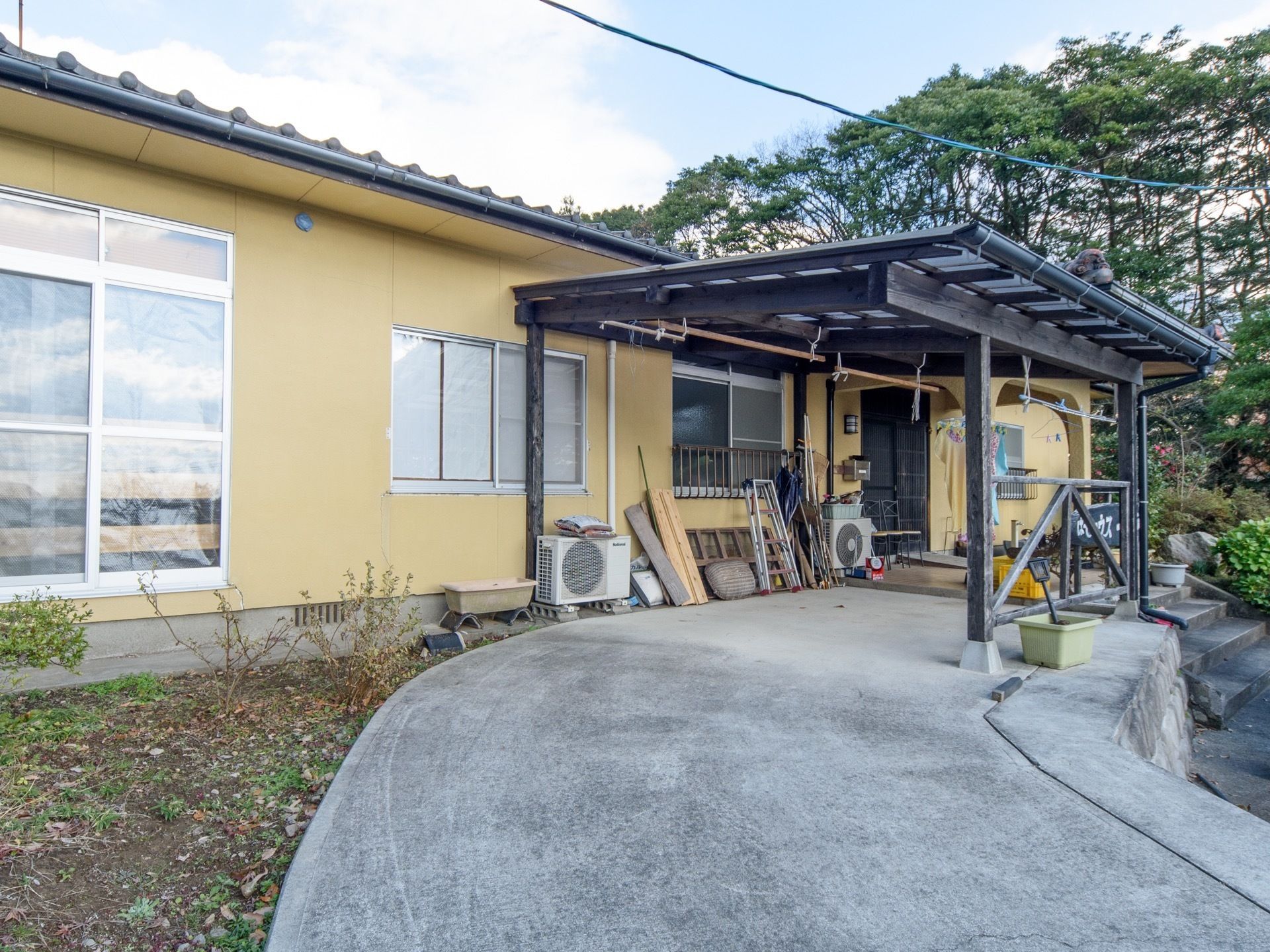 屋根が付いており、洗濯干しができるようになっている。コンクリートのスロープが手前側に伸びている。エアコンの室外機が２台ある。