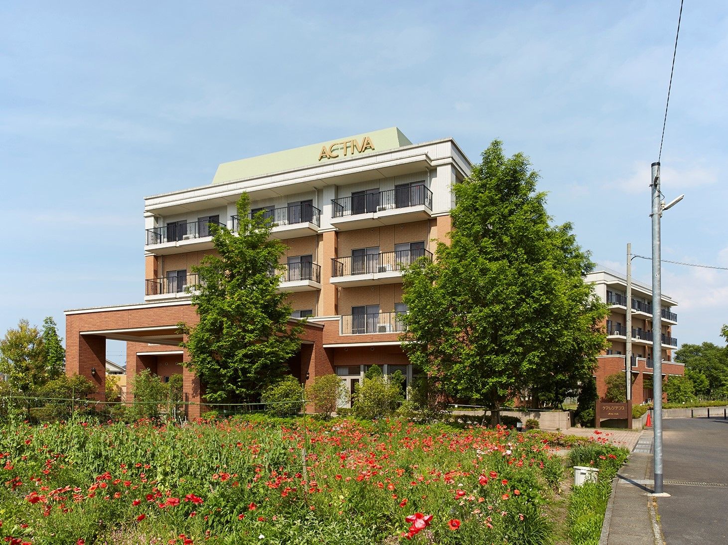 緑に囲まれた、レンガ色と白の外壁が印象的なマンション風の建物。全部で８棟300室、20タイプの居室からお選びいただける。