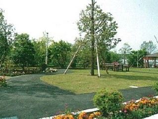 芝生の敷かれた庭の上には、アウトドアテーブルがあり、背の高い照明も付いている。奥には屋根のついた東屋が見える。