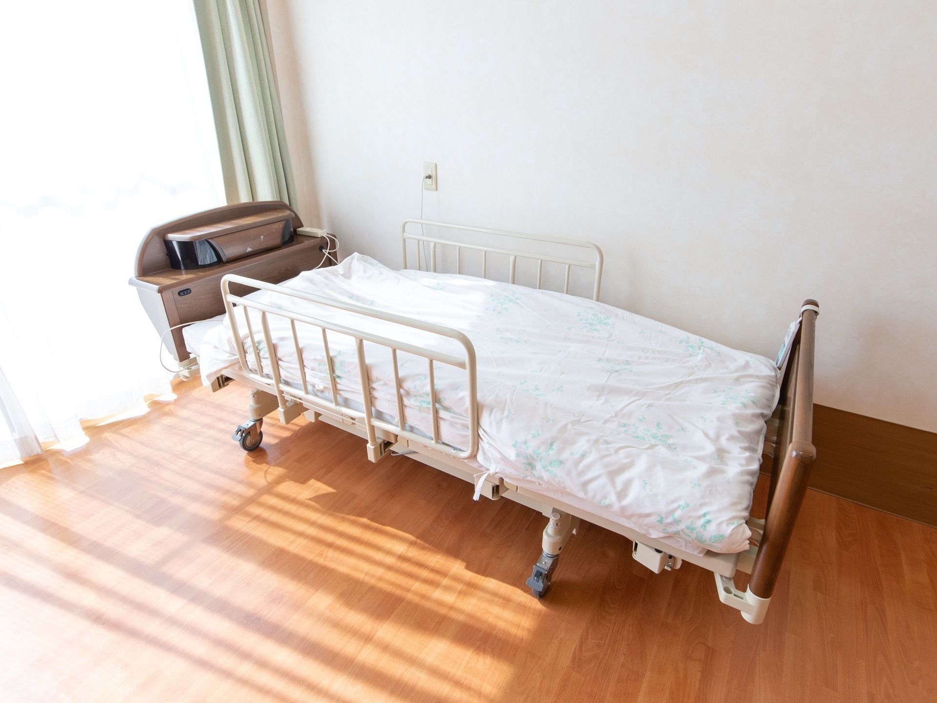 転倒防止柵の付いた移動式の介護ベッドが置かれている。大きな窓からは日がたっぷり差し込んでいる。フローリングである。