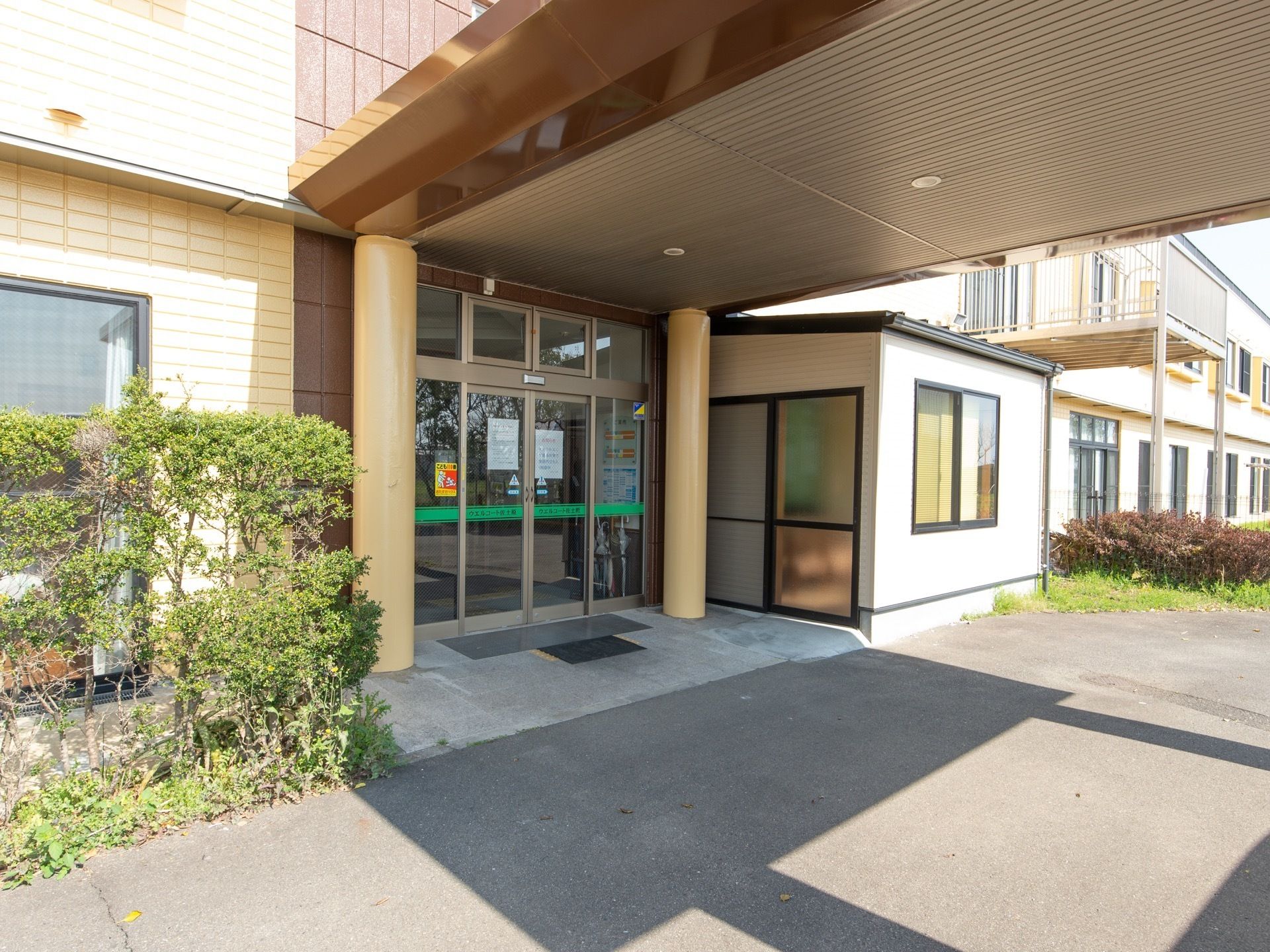玄関前の通路には屋根が設けられている。玄関は自動ドアとなっている。周囲には木が植えられて、緑を感じることができる。