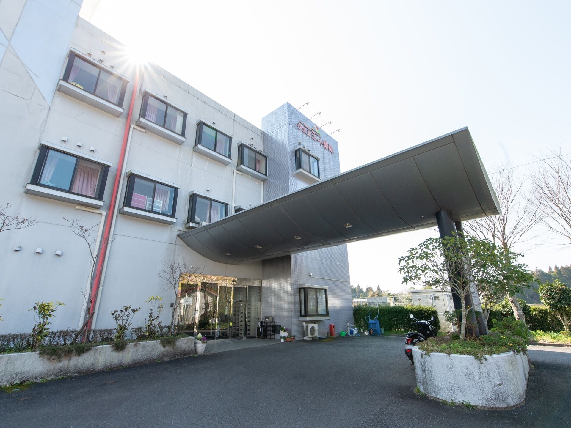 エントランス前は大きな屋根があり、ゆるやかなスロープも設けられている。周囲には植木などが植えられている。