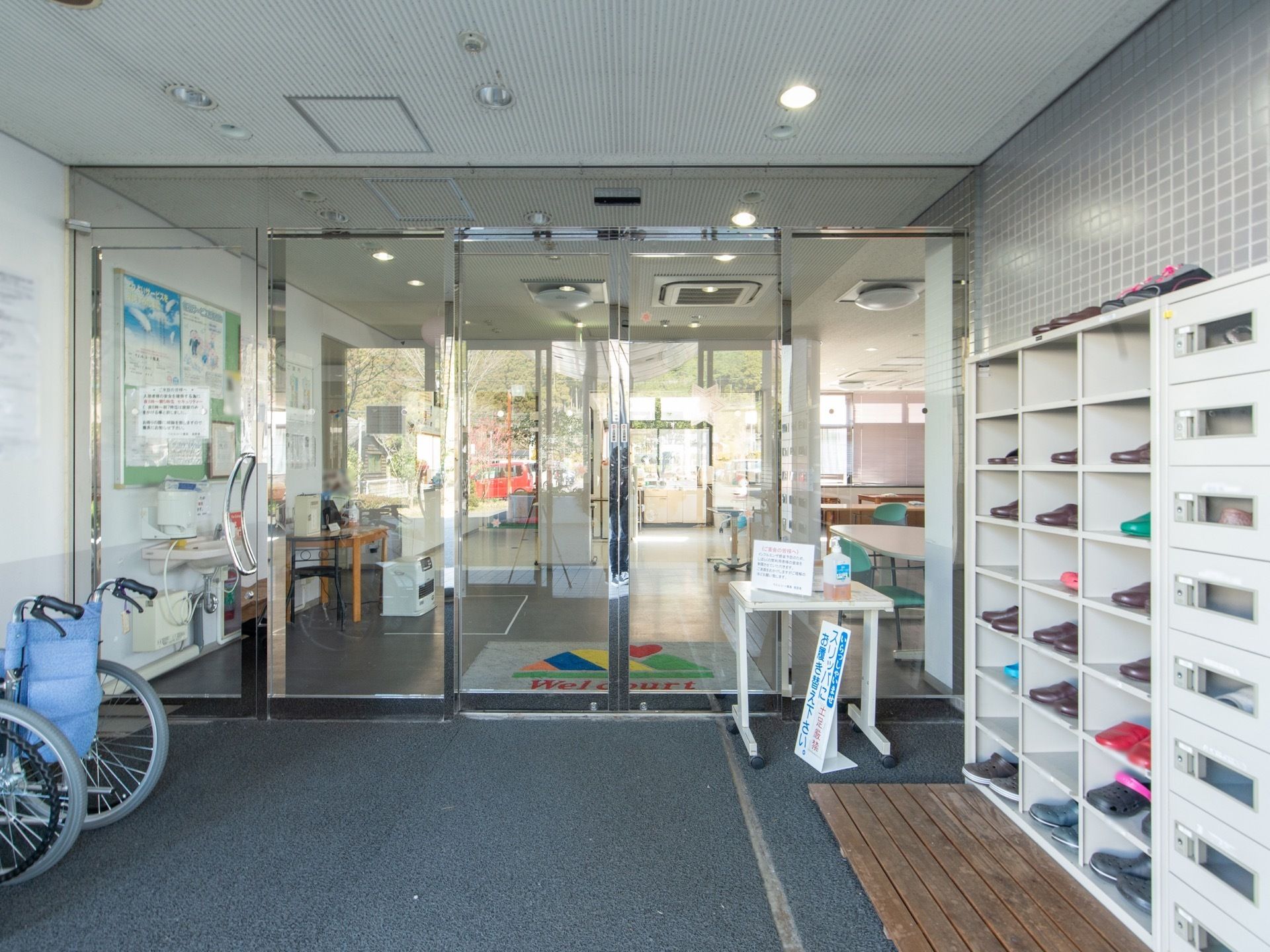 風除室内には下駄箱が置かれている。手指用消毒スプレーが置かれ、感染予防に配慮している。バリアフリーの造りである。