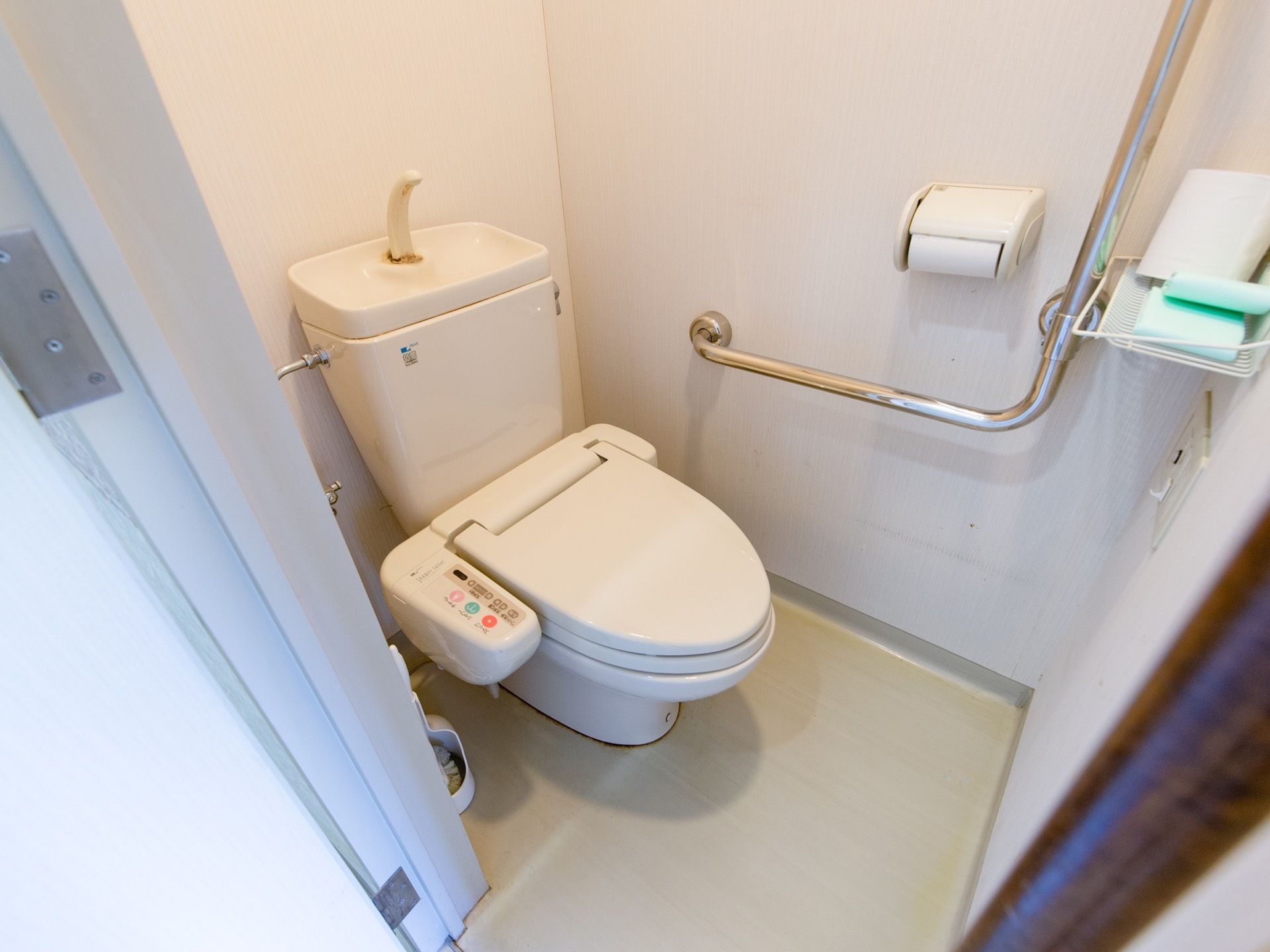 暖房便座洗浄機能付きトイレで、壁には手すりが取りつけてある。壁は白色、床はアイボリーの配色の内装である。