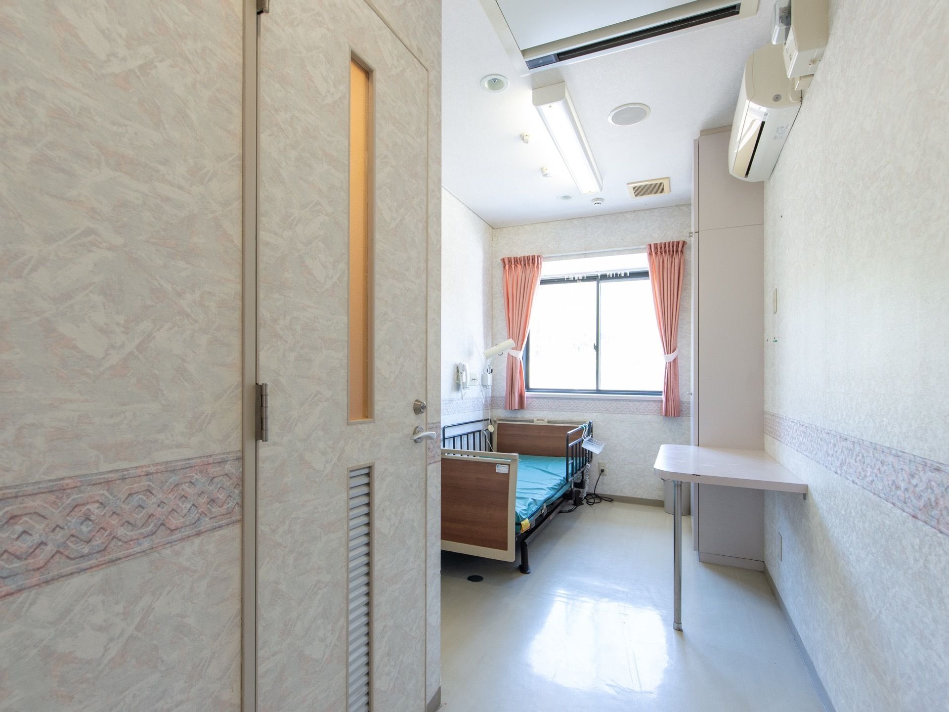 ピンク色のカーテンがかけられた腰高窓があり、明るい雰囲気である。居室内には専用のトイレが完備してある。
