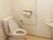 トイレには温水洗浄便座が設置され、周囲には手すり、緊急呼出ボタン、手洗いの流しがある。白を基調とした明るい空間である。